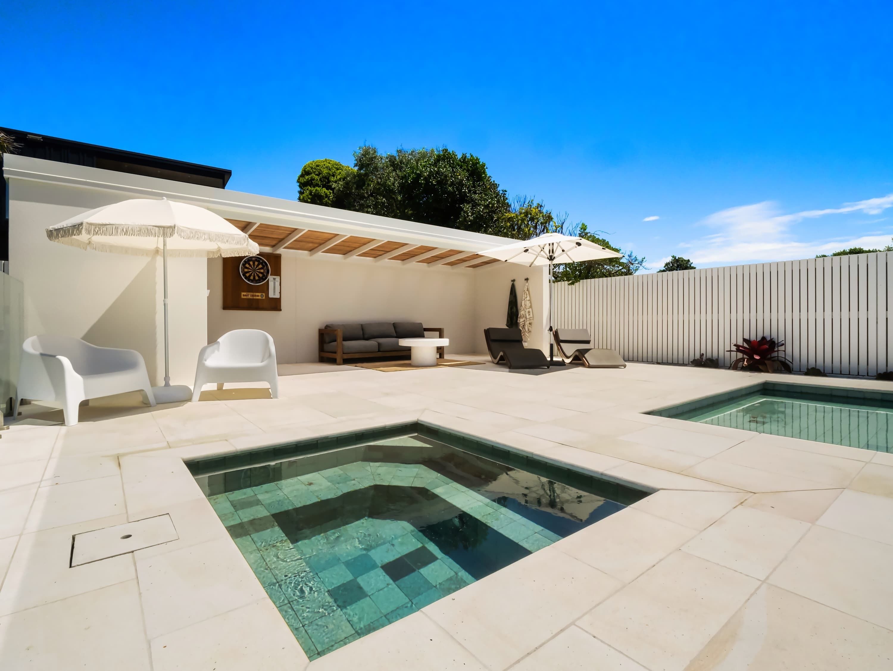 A modern outdoor pool area with a pergola, lounge chairs, and a dining table.