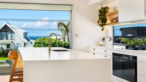 Een moderne keuken met een groot eiland, een ingebouwde oven en uitzicht op een huis en groen.