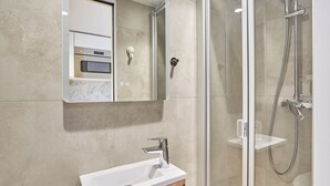 A modern bathroom with a glass shower enclosure, a white sink, and a mirror above it. - Charming Studio - Louvre & Palais Royal (Paris)