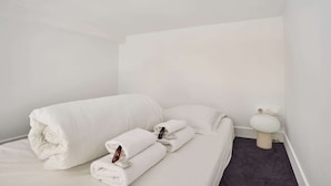 A hotel room with a neatly made bed, two pillows, a folded towel, and a white toilet. - Charming Studio - Louvre & Palais Royal (Paris)