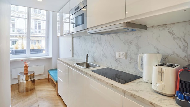 A modern kitchen with white cabinets, a marble countertop, a built-in oven, a sink, a kettle, and a toaster. - Charming Studio - Louvre & Palais Royal (Paris)