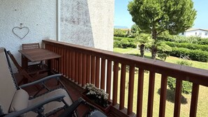 En balkon med et træbord og stole, en hjerteformet dekoration og udsigt over en velplejet have med et stort træ.