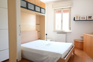 Une chambre à coucher avec un lit, une armoire, un radiateur, une fenêtre et une table de chevet.