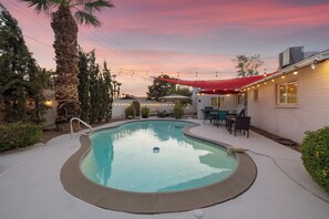 A swimming pool with a red canopy and string lights, surrounded by patio furniture and palm trees. - Tempe Delight with Heated Pool (Tempe)