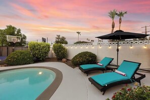 A swimming pool with lounge chairs and an umbrella, surrounded by greenery and a basketball hoop. - Tempe Delight with Heated Pool  (Tempe)