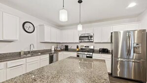 Une cuisine moderne avec des meubles blancs, un plan de travail en granit, des appareils électroménagers en acier inoxydable et des luminaires suspendus.