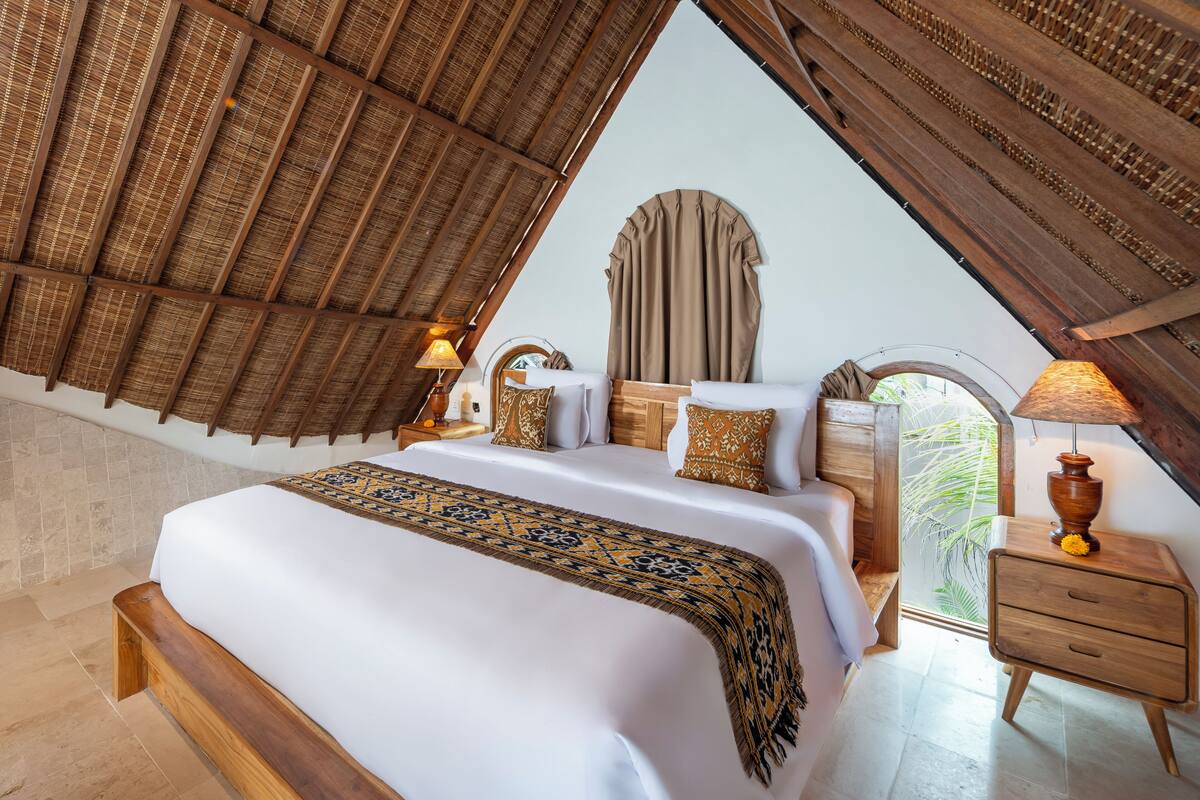A bedroom with a large bed, wooden headboard, and a window with a view of greenery.