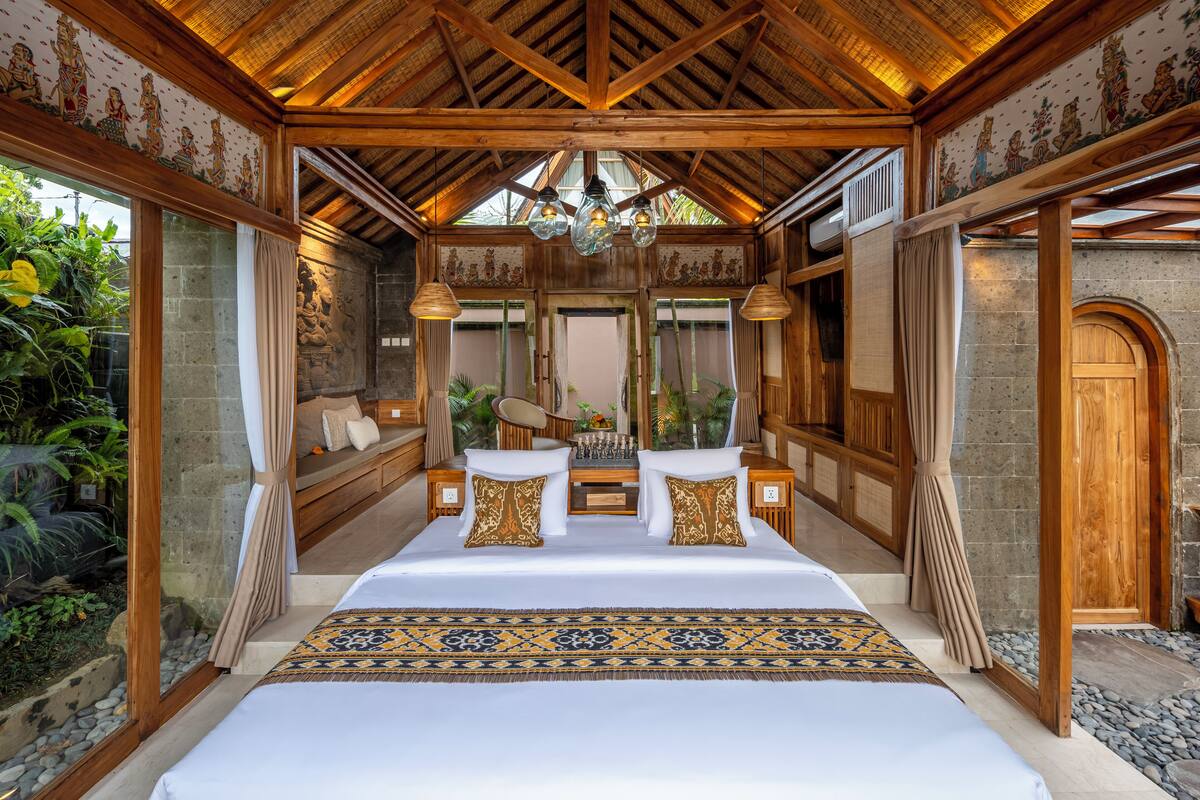 A spacious bedroom with a large bed, wooden ceiling beams, and a view of the outdoors.
