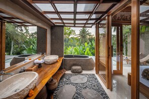 A modern bathroom with a wooden vanity, stone sinks, and a view of lush greenery. - Govala Usada Ubud Villa (Tegallalang)
