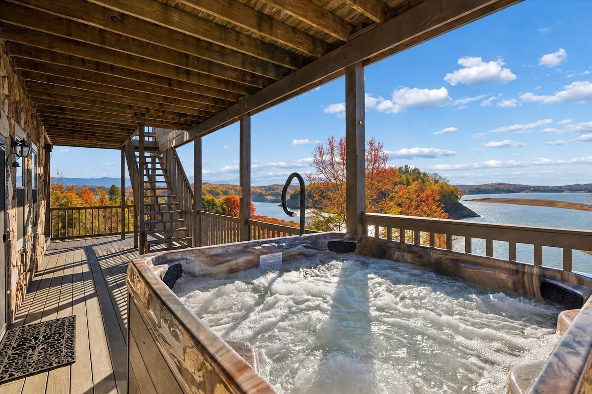 A wooden deck with a hot tub, overlooking a lake with autumn foliage.
