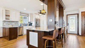 A modern kitchen with white cabinets, a marble island, and a bar area with stools.