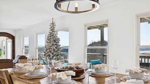 A dining room with a Christmas tree, a chandelier, and a view of the outdoors.