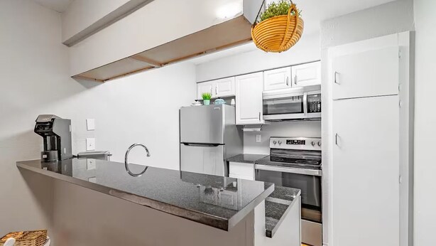 Eine moderne Küche mit weißen Schränken, einem Edelstahl-Kühlschrank, einer Mikrowelle und einem Herd.