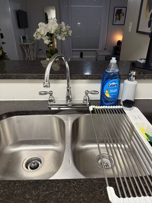 Una cocina con un fregadero de acero inoxidable, una botella de detergente Dawn y un escurreplatos.