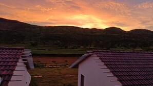 A view of a valley with a sunset, featuring a building with a red-tiled roof and a white facade. - Double Room #1 (Igatpuri)