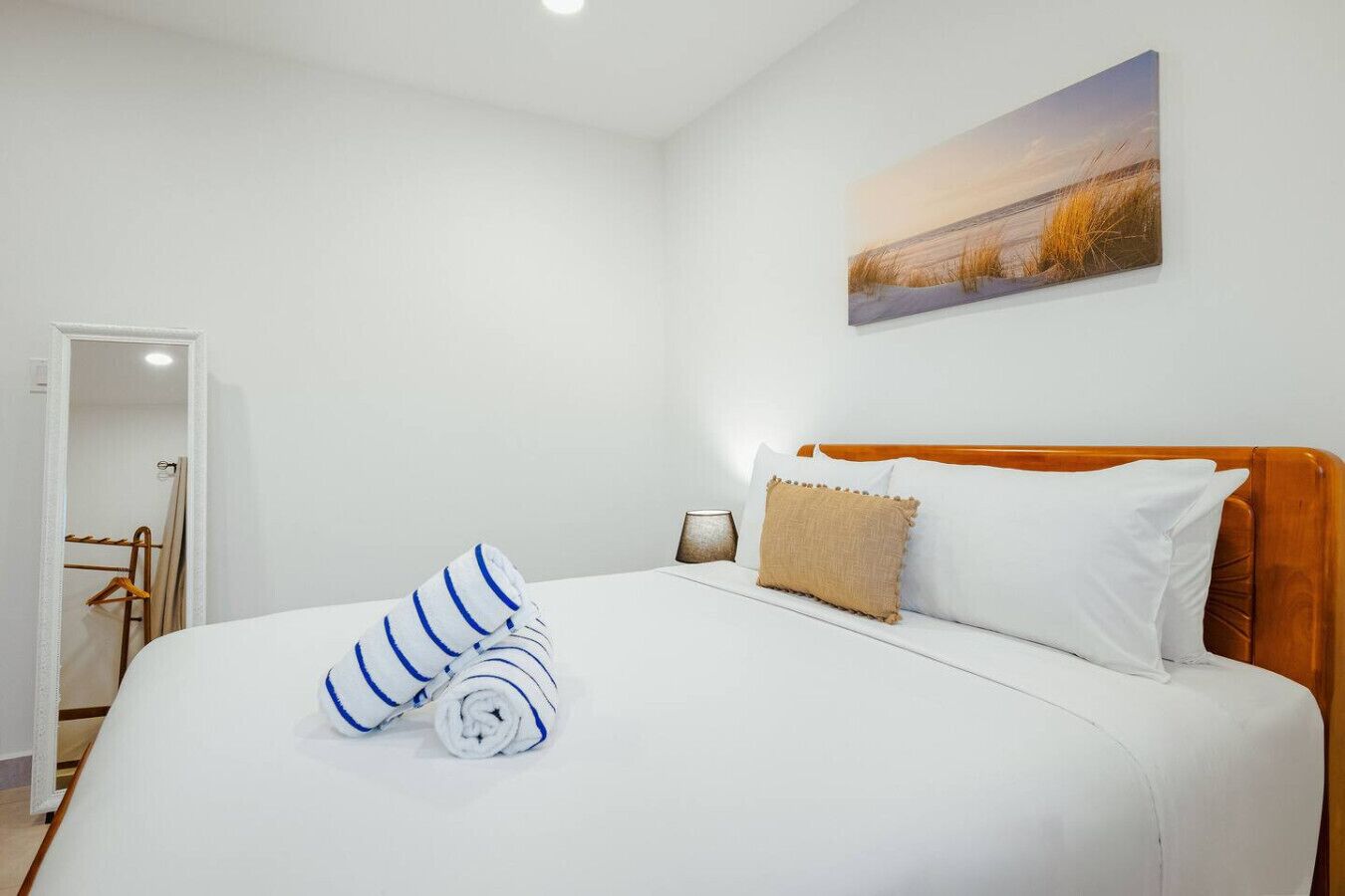 Een netjes opgemaakt bed met witte en blauw gestreepte handdoeken, een houten hoofdbord en een schilderij van een landschap aan de muur.