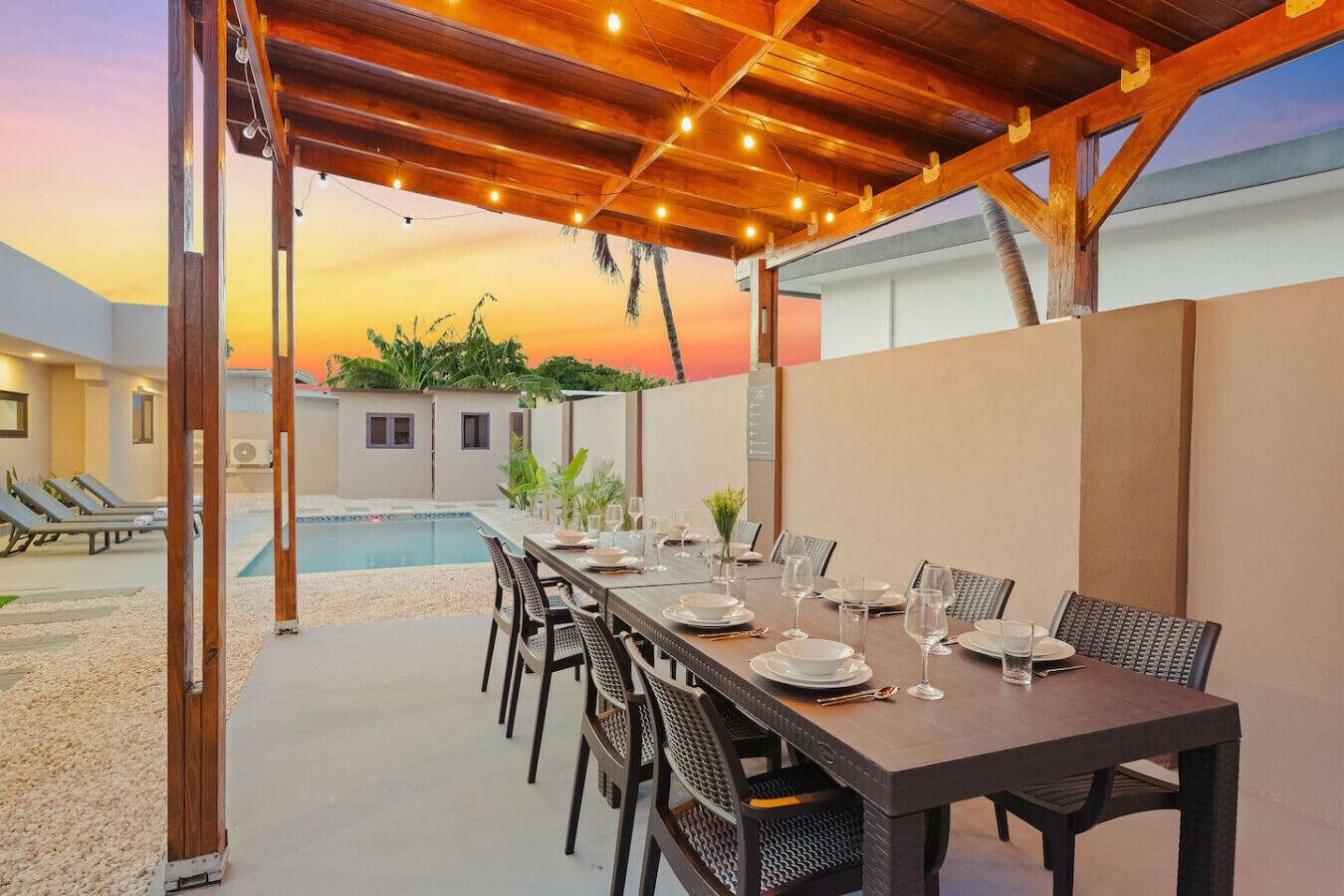 Un espace extérieur aménagé pour les repas, avec une piscine, un pergolas en bois qui le recouvre, et une vue imprenable sur le coucher de soleil.