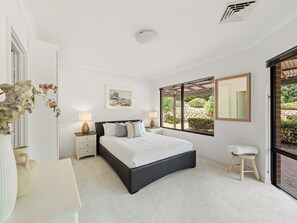 A bedroom with a large bed, bedside tables, a window with a view, and a small stool. - Sailors Hill Retreat—Bushland Living by the Coast (Naturaliste)