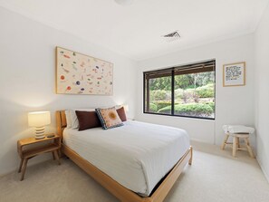 A bedroom with a large bed, a bedside table with a lamp, a window with a view of greenery, and a wall with a framed quote. - Sailors Hill Retreat—Bushland Living by the Coast (Naturaliste)