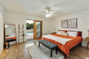 Ein Schlafzimmer mit Bett, einer Bank, einem Deckenventilator, einem großen Fenster und Bildern an der Wand.
