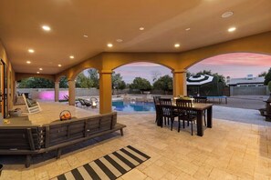Eine Außenpatio mit Pool, Sitzbereichen und einem überdachten Bereich mit Tischen und Stühlen.