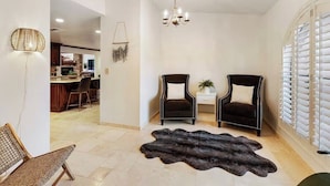 Un salon moderne avec deux fauteuils en cuir foncé, un fauteuil en osier, un tapis en fourrure et un lustre.