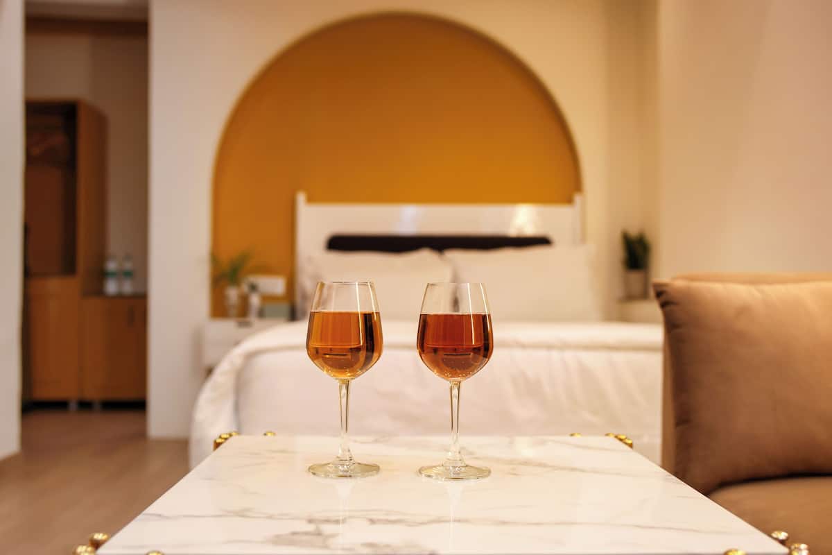 A hotel room with a marble table, two glasses of wine, a bed, and a sofa.