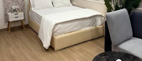 A modern bedroom with a bed, bedside table, chair, and a small round table with a remote control.