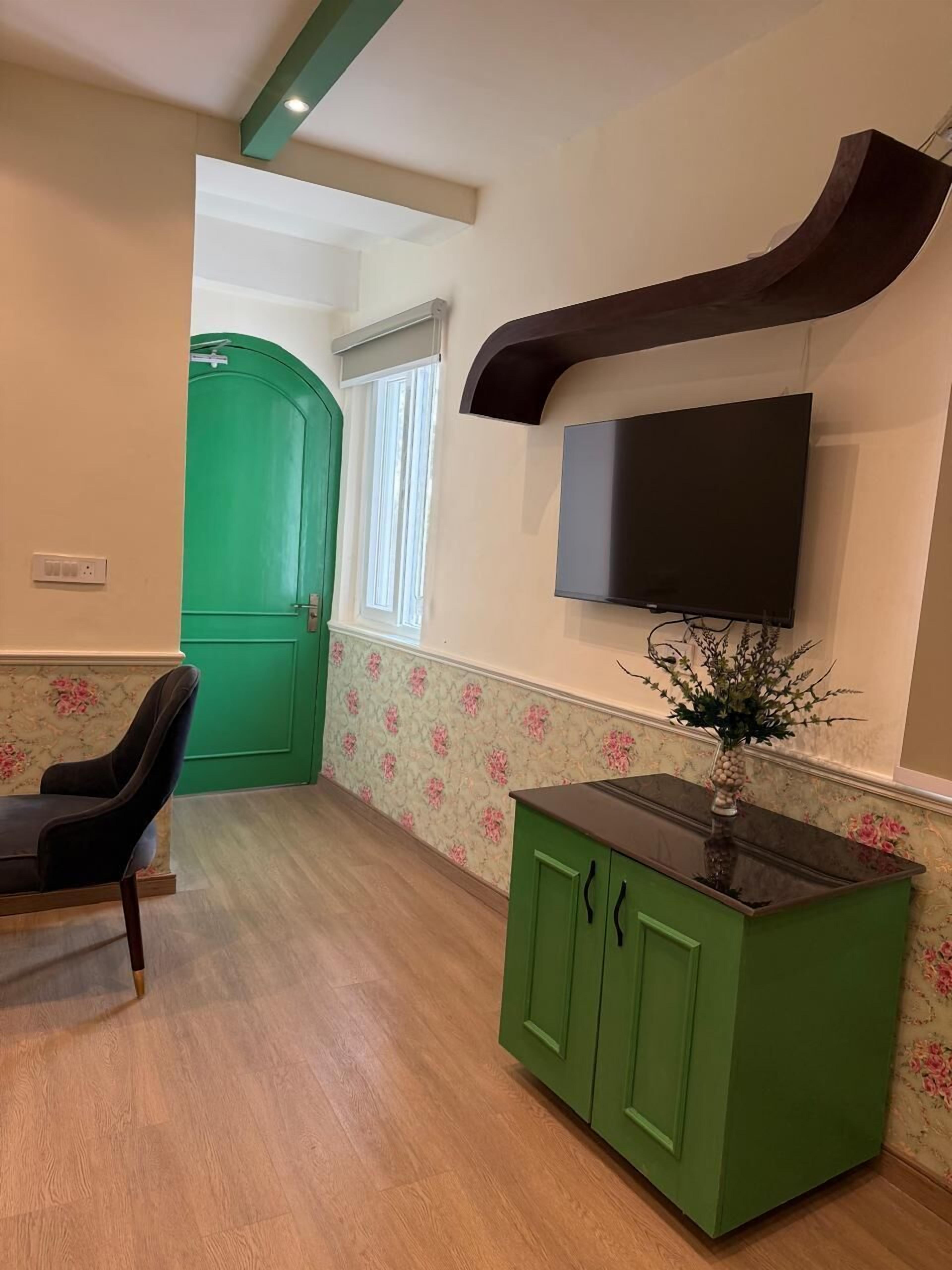 A room with a green door, a flat-screen TV mounted on the wall, a wooden floor, and a green cabinet.