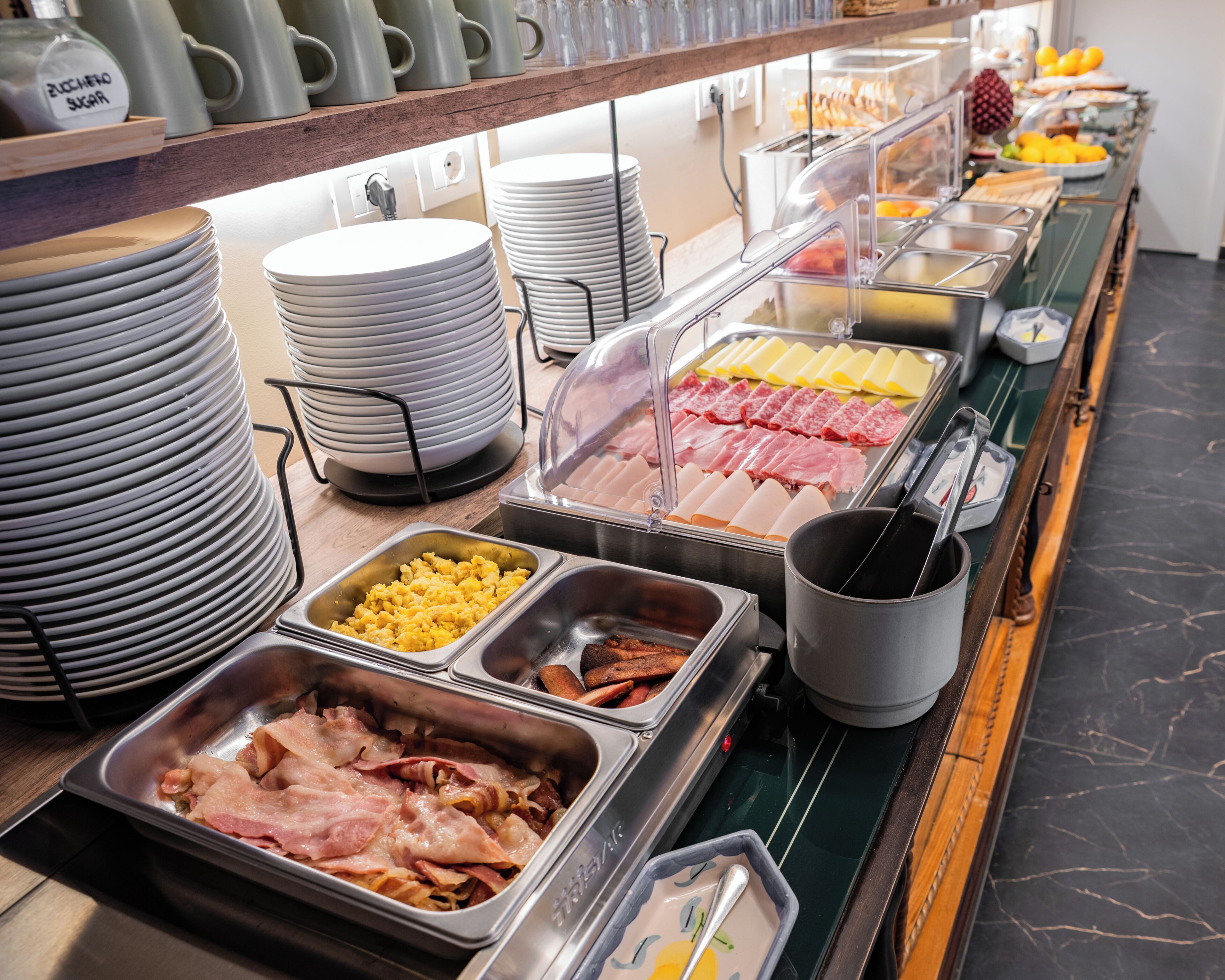 A buffet with various food options including meats, cheeses, and fruits.