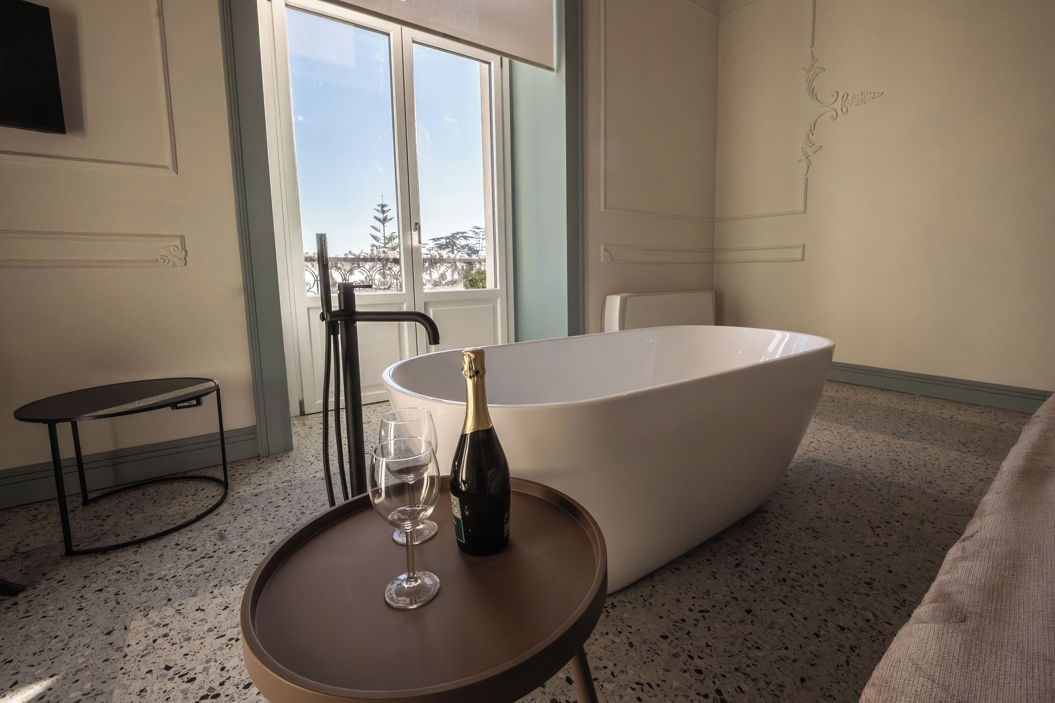 Una habitación con una bañera, una botella de champán y dos copas sobre una mesita.