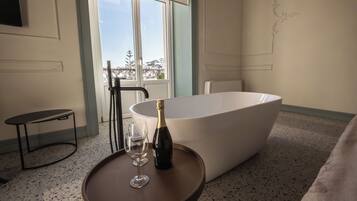 Una habitación con una bañera, una botella de champán y dos copas sobre una mesita.