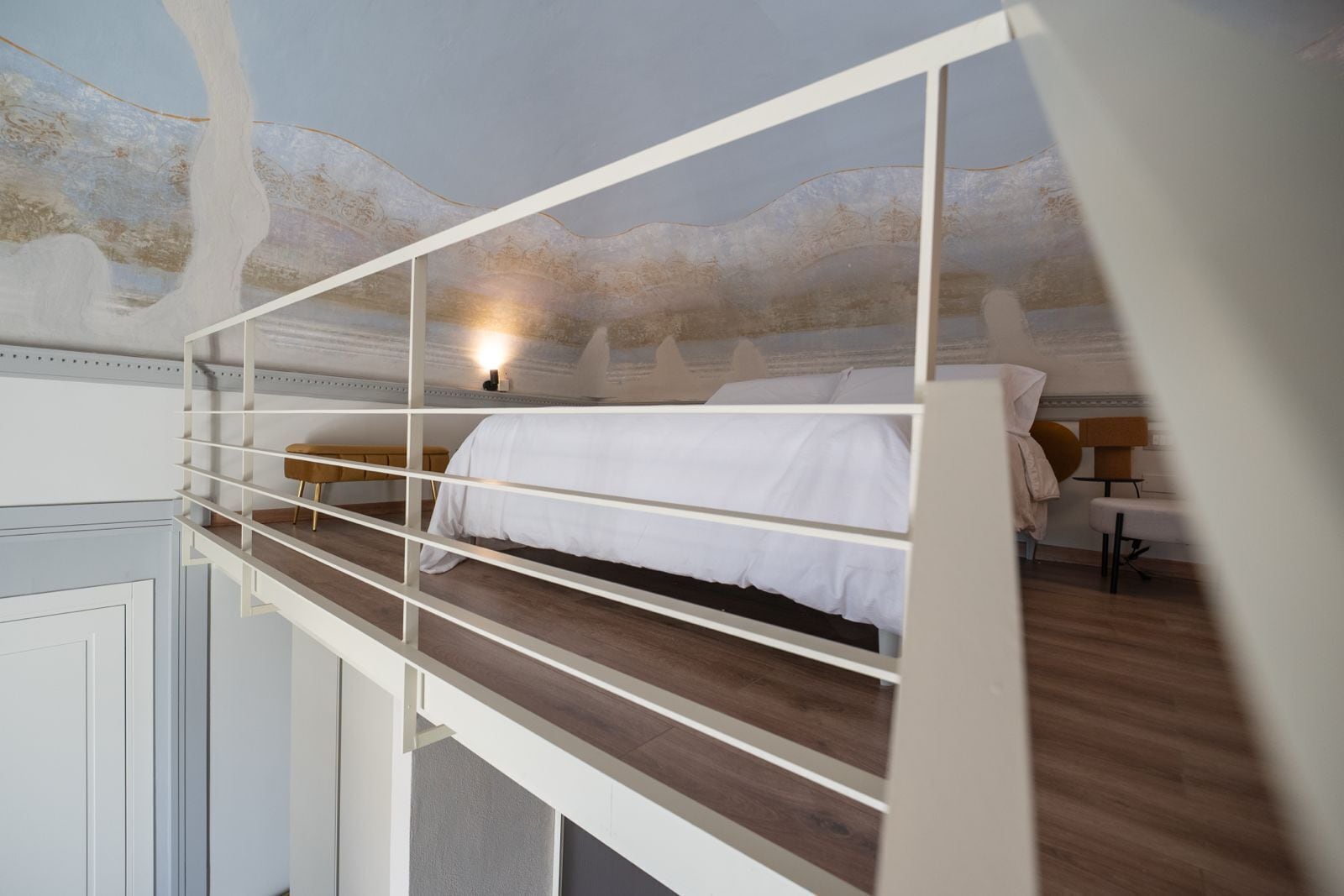 A bunk bed with a white headboard, a bedside table with a lamp, and a wall with a decorative pattern.