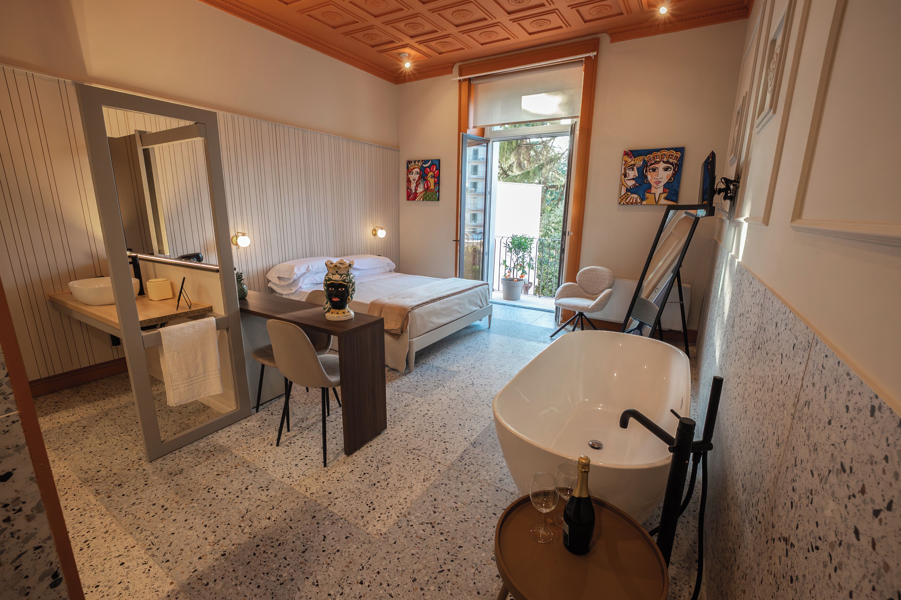 A modern bathroom with a freestanding bathtub, a large mirror, and a bedside table with a bottle and glasses.