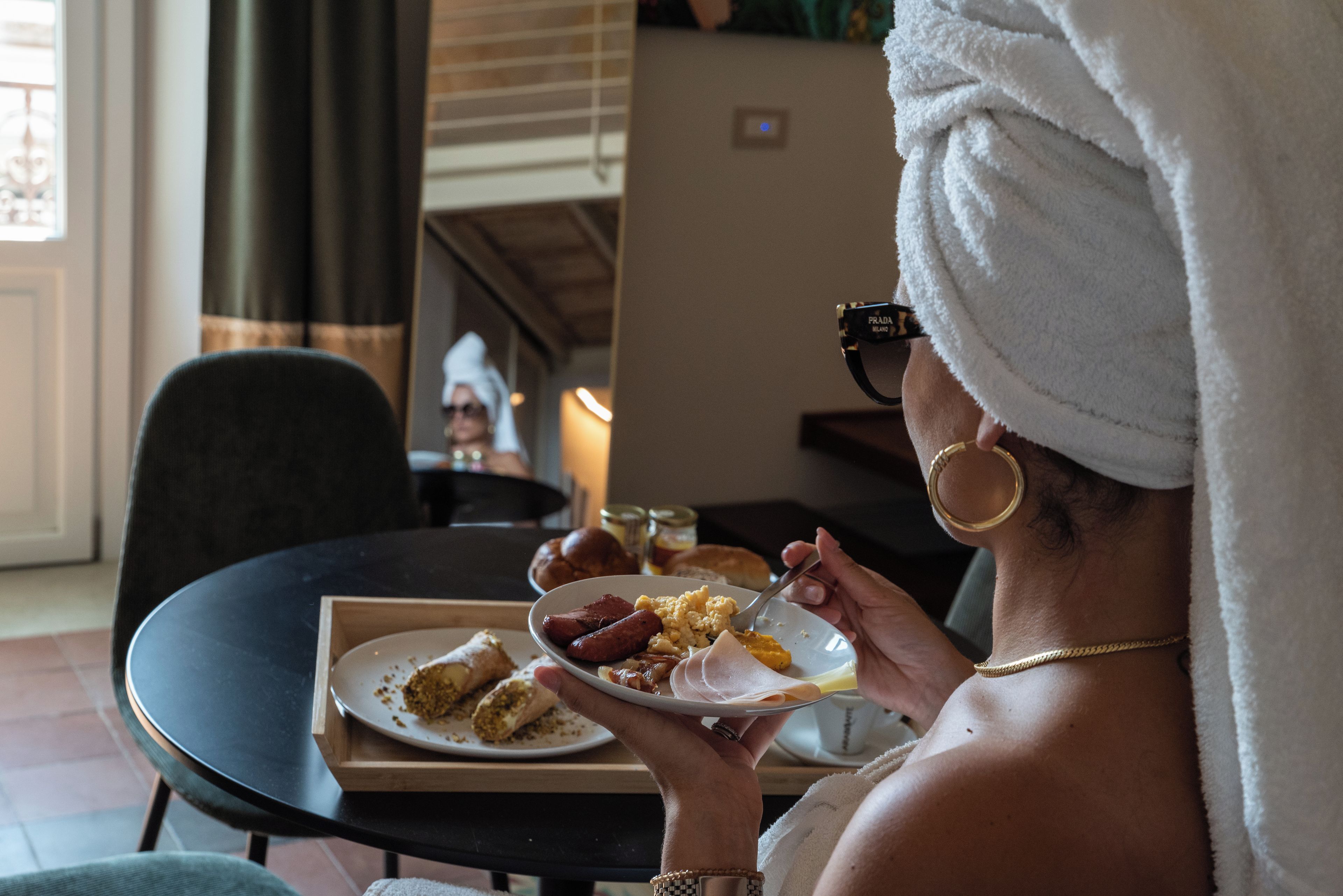 Uma pessoa com uma toalha na cabeça, segurando uma bandeja com comida e bebida.