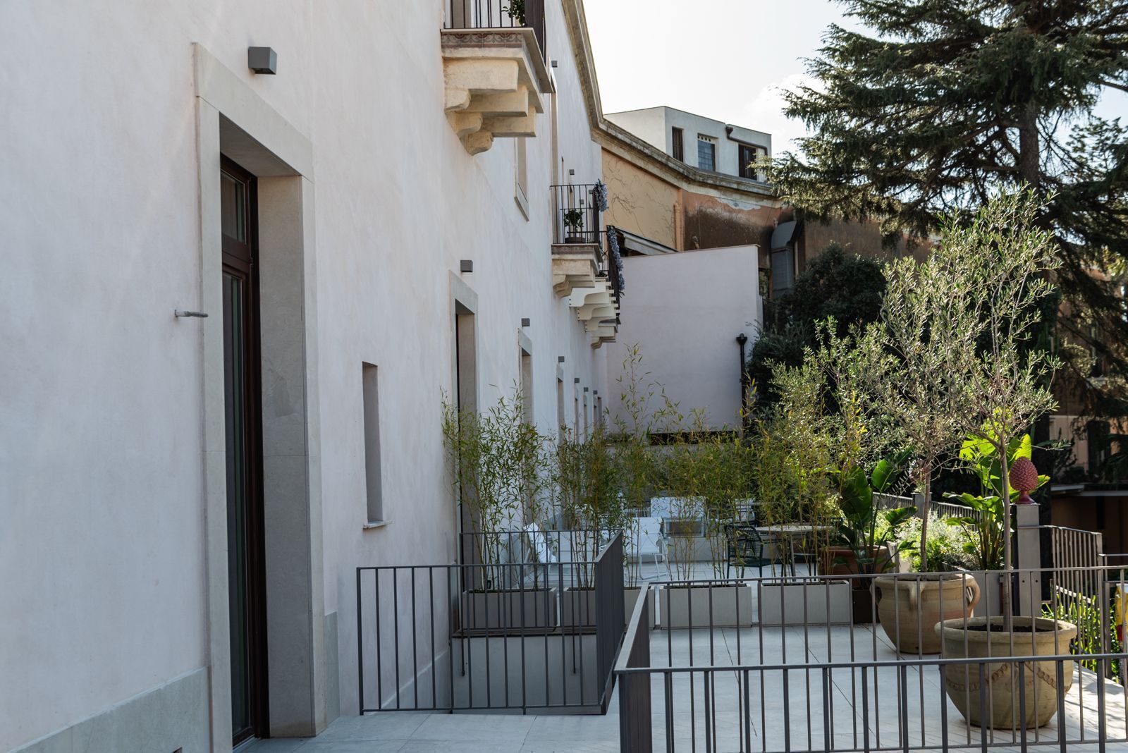 A narrow urban courtyard with a white building, a metal fence, and potted plants.