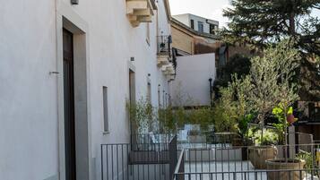 A narrow urban courtyard with a white building, a metal fence, and potted plants.