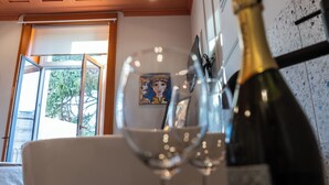 A room with a bed, a window with a view of trees, a painting on the wall, and a bottle of champagne. - Des Bains Chambre & Suite (Acireale)