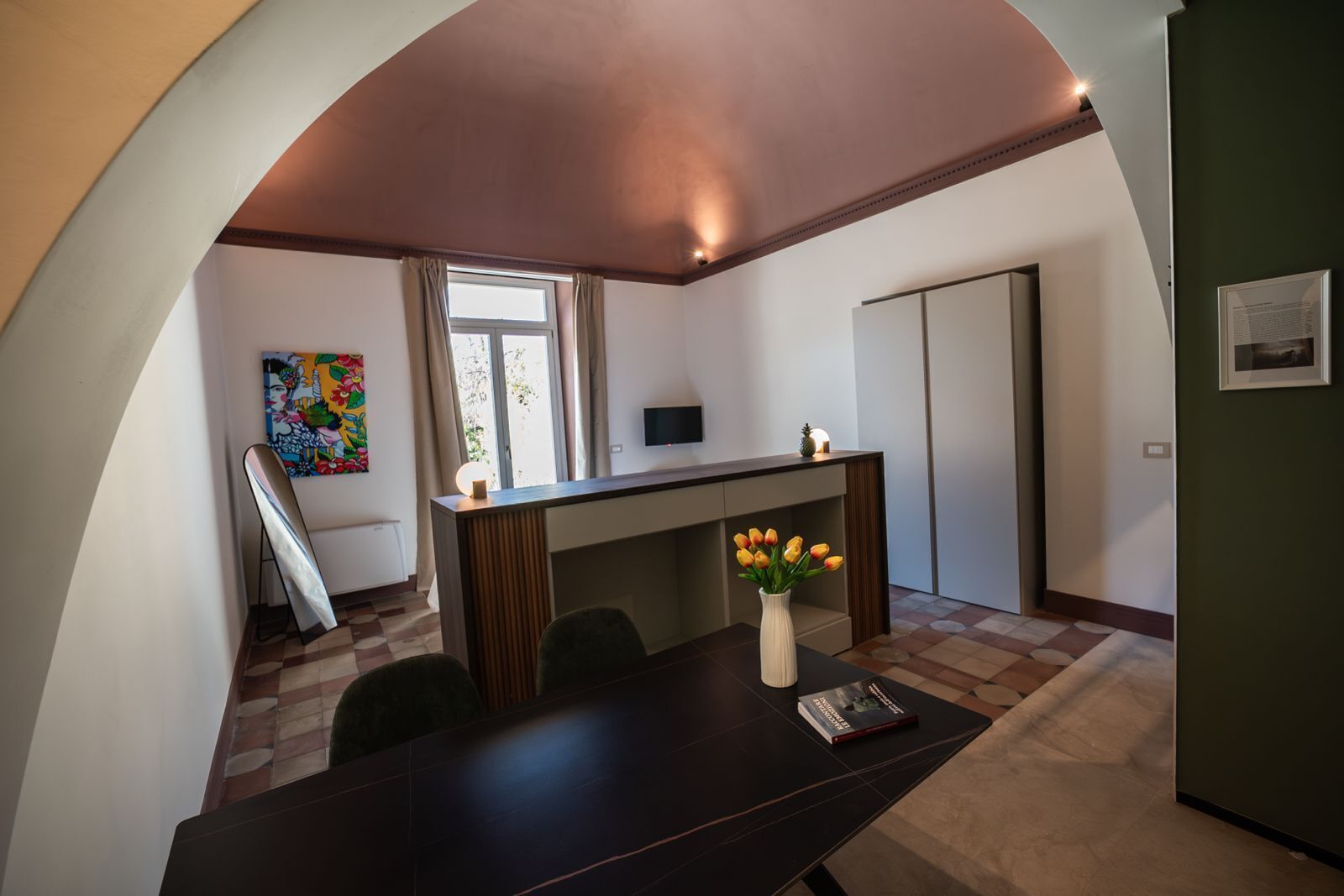 A modern room with a dark wooden desk, a vase of tulips, and a colorful abstract painting on the wall.