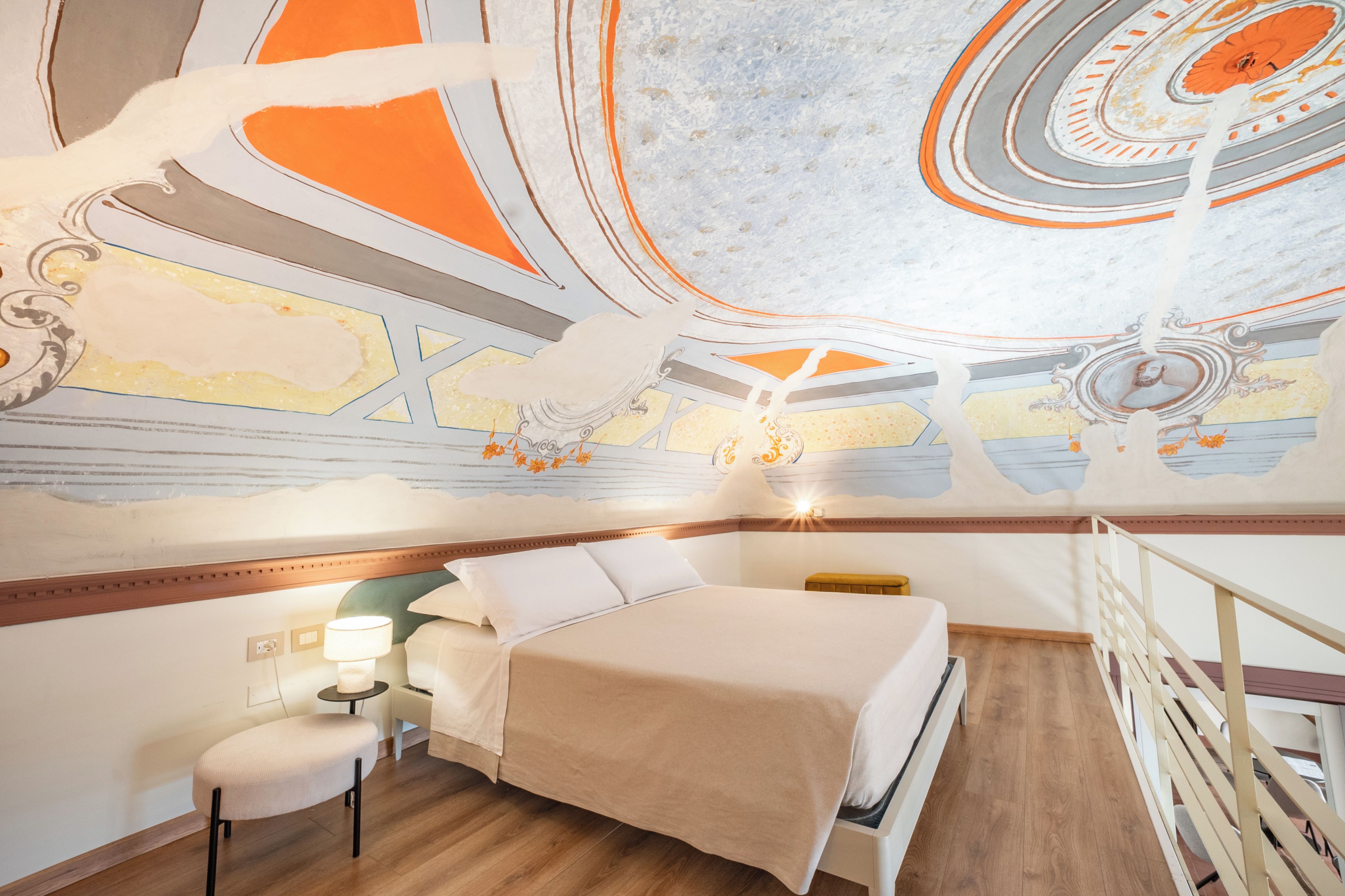 A hotel room with a bed, a nightstand, a lamp, and a view of the ceiling with a mural.