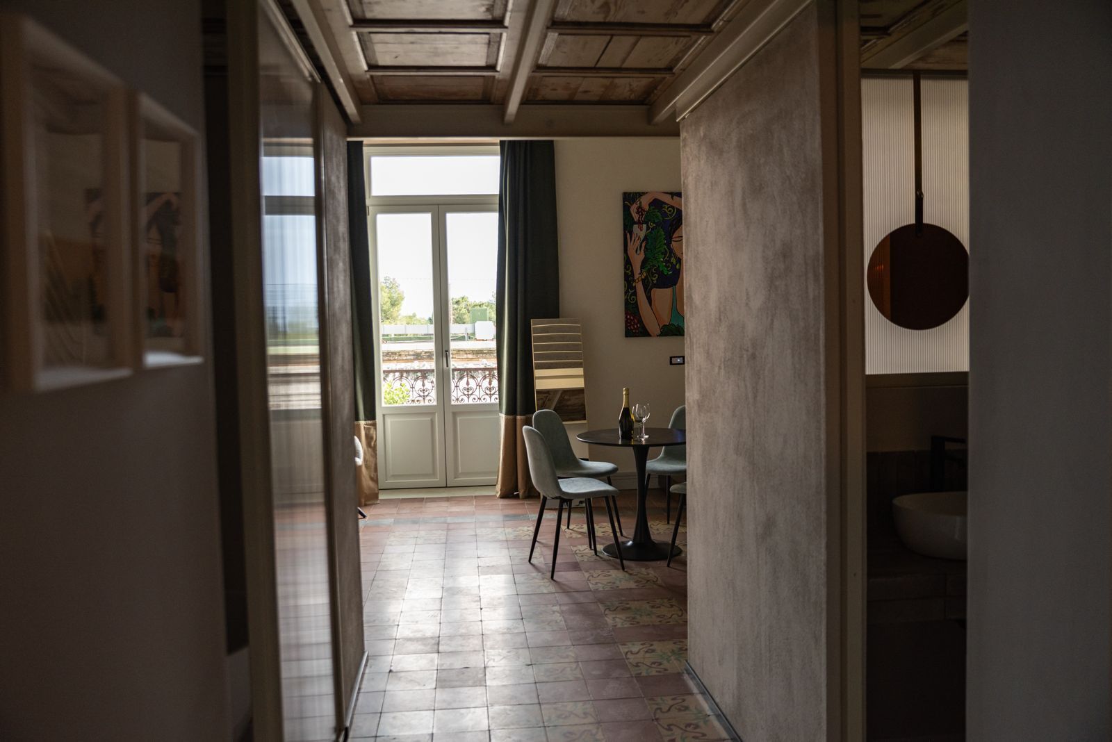 A hallway leading to a dining area with a table set for two, a painting on the wall, and a view through a glass door.