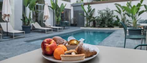 A dining table with a plate of food, a swimming pool, and outdoor seating.