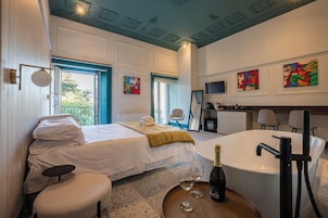 Camera d'albergo con un letto, una zona salotto, una vasca da bagno e opere d'arte alle pareti.