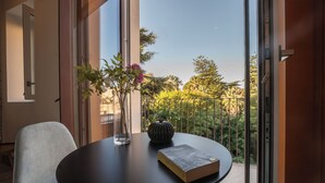 A modern room with a round table, a chair, a book, a vase with flowers, and a view of greenery outside. - Des Bains Chambre & Suite (Acireale)