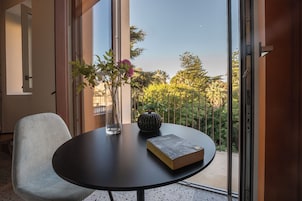 Una stanza moderna con un tavolo rotondo, una sedia, un libro, un vaso con fiori e vista sul verde circostante.