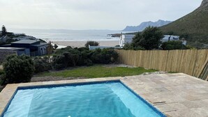 Una piscina rectangular con agua cristalina azul, rodeada por una terraza de piedra y una valla de madera.