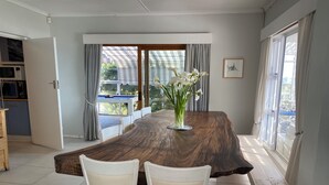 Un comedor con una gran mesa de madera, dos sillas blancas y un jarrón de flores.