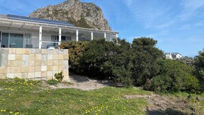 Un edificio moderno con fachada de piedra, paneles solares y vista a una montaña rocosa.