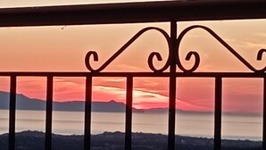 Ein Balkongeländer mit Blick auf einen Sonnenuntergang über einem Gewässer und entfernte Berge.