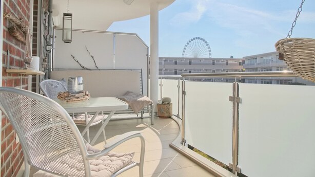 En balkon med et bord og stole, en hængende lampe, udsigt til et pariserhjul og en murstensvæg.